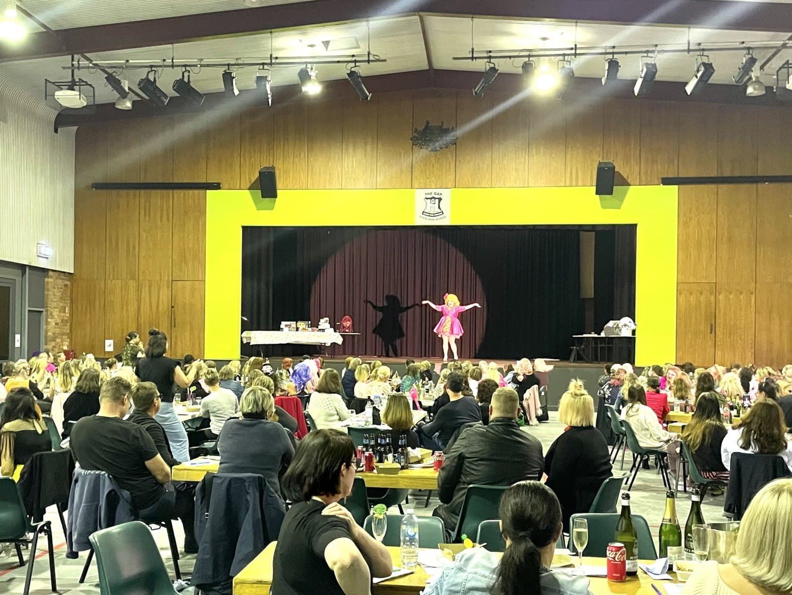 Mother's Day high tea: a performer in pink on stage in front of a yellow frame, watched by guests at their tables